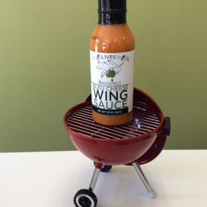 A bottle of wing sauce sitting on top of an outdoor grill.